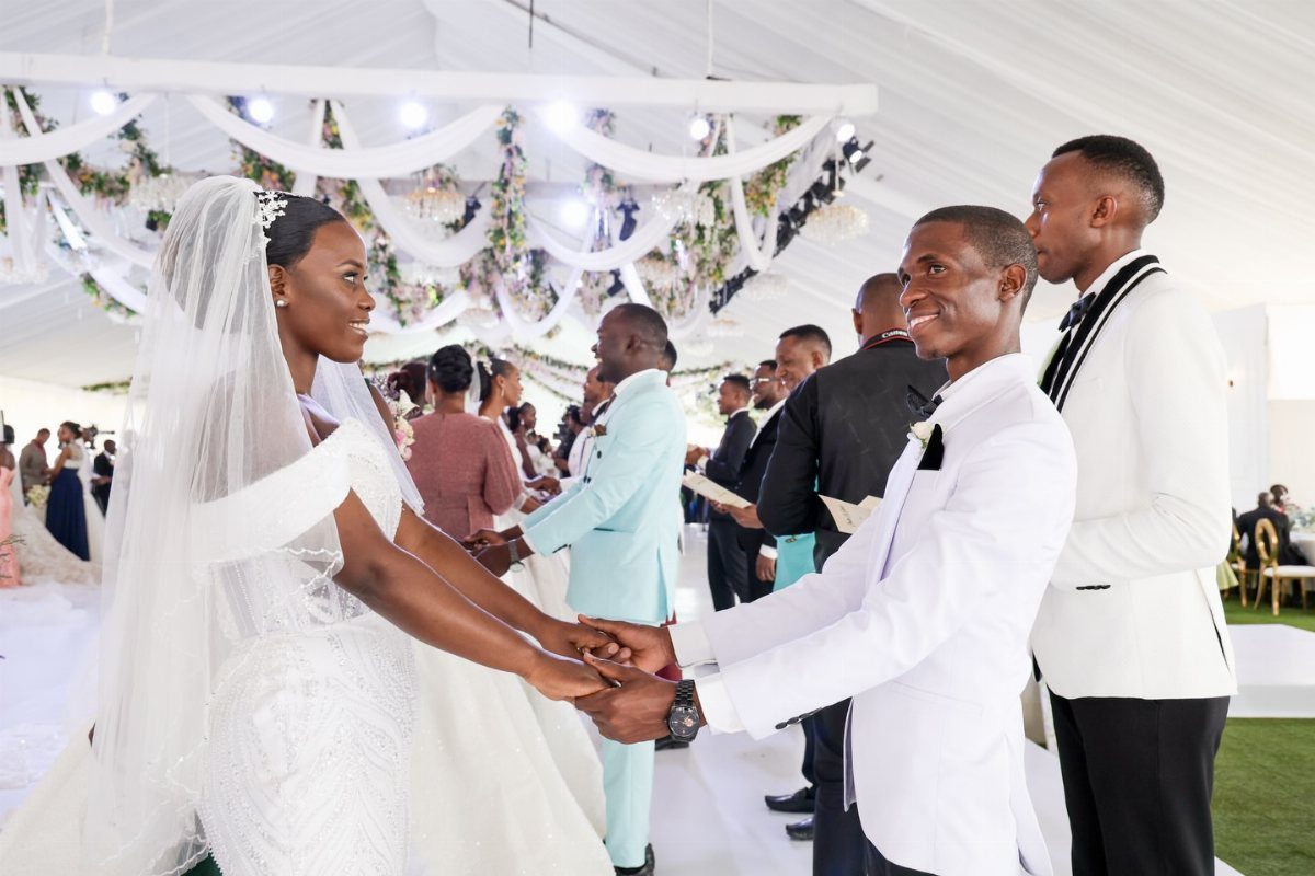 Bride in white lace gown and groom in white tuxedo holding hands at wedding