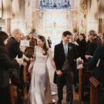 Bride in a white A-line wedding dress and groom walking through a church aisle.