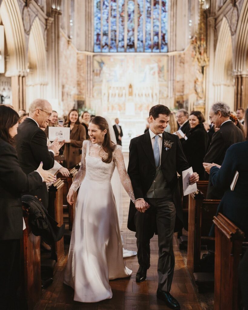 Bride in a white A-line wedding dress and groom walking through a church aisle.