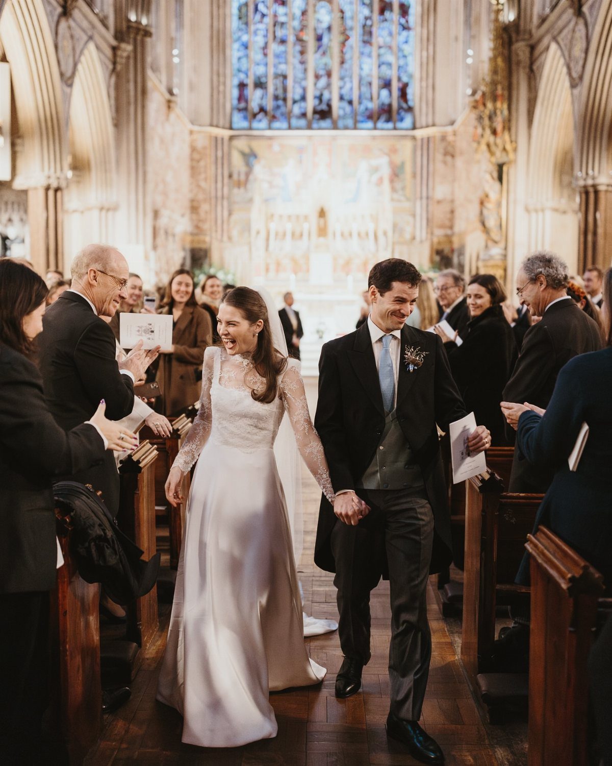 Bride in a white A-line wedding dress and groom walking through a church aisle.