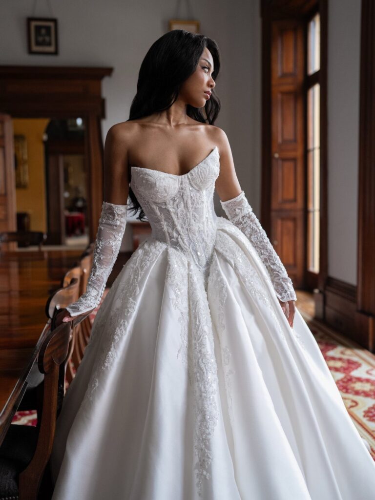Woman in a white wedding dress with a structured basque waist and lace gloves.