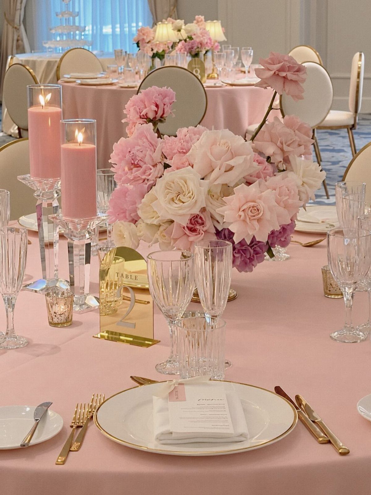 Pink wedding table setting with gold cutlery and a bouquet of pink roses.