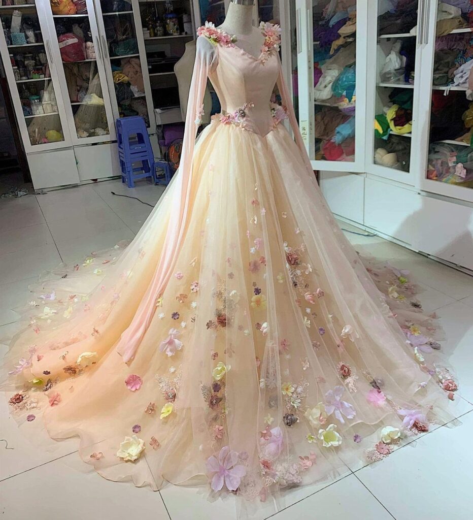 Pale peach wedding gown with 3D floral appliqués on a mannequin in a studio