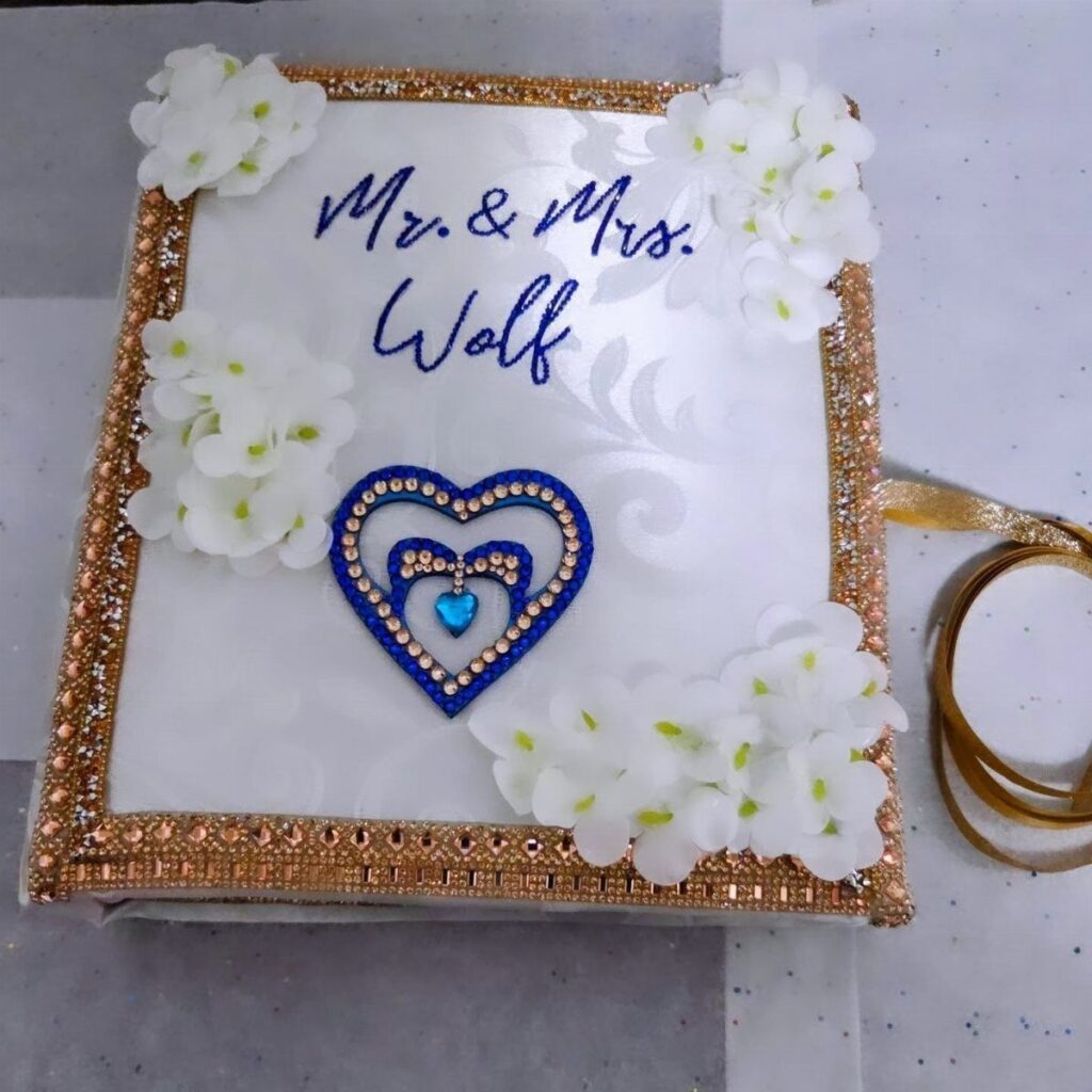 White personalized photo album cover with gold rhinestones, blue heart, and white flowers.