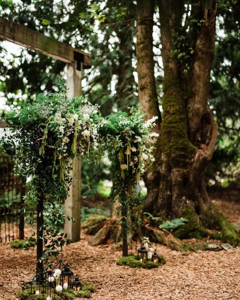 Floral wedding arbor with white flowers and lanterns in a mossy forest setting