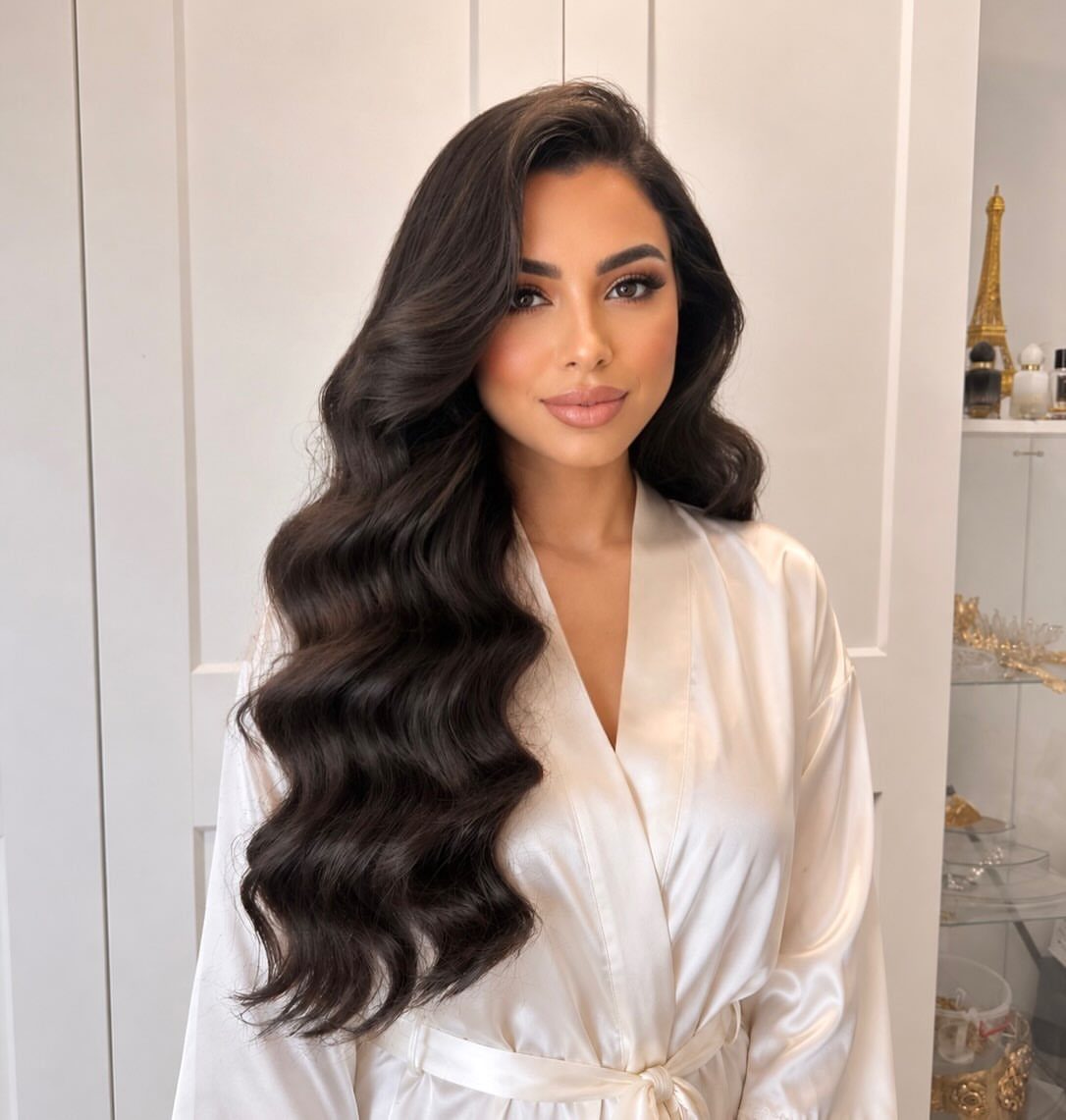 Woman with long dark hair styled in voluminous polished waves wearing white satin robe