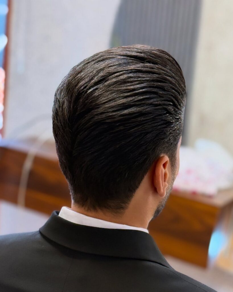 Man with slicked-back dark hair wearing a black suit and white shirt.