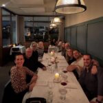 Group of friends smiling while sitting around a long dinner table in a restaurant