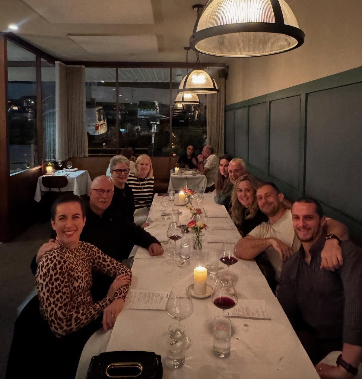 Group of friends smiling while sitting around a long dinner table in a restaurant