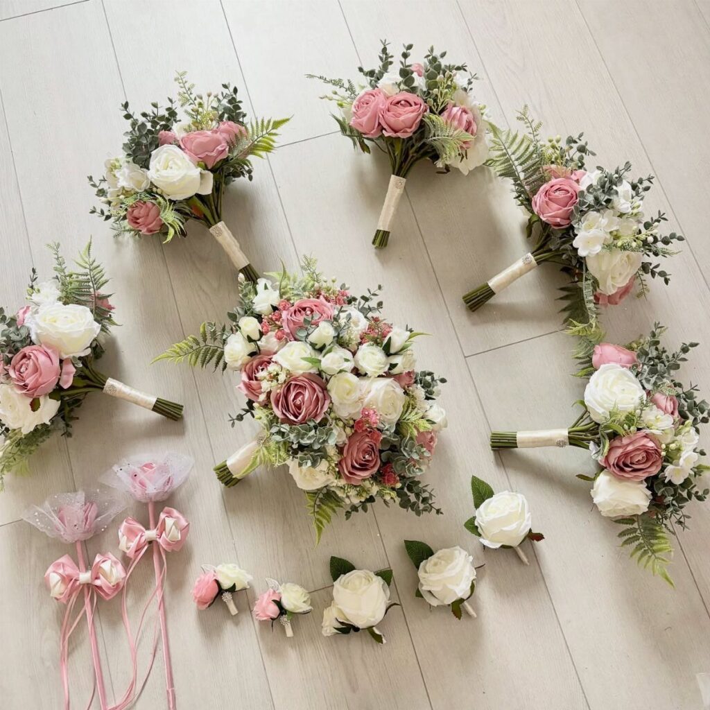 Dusty rose and white rose bridal bouquets and boutonnieres on a light wooden floor.