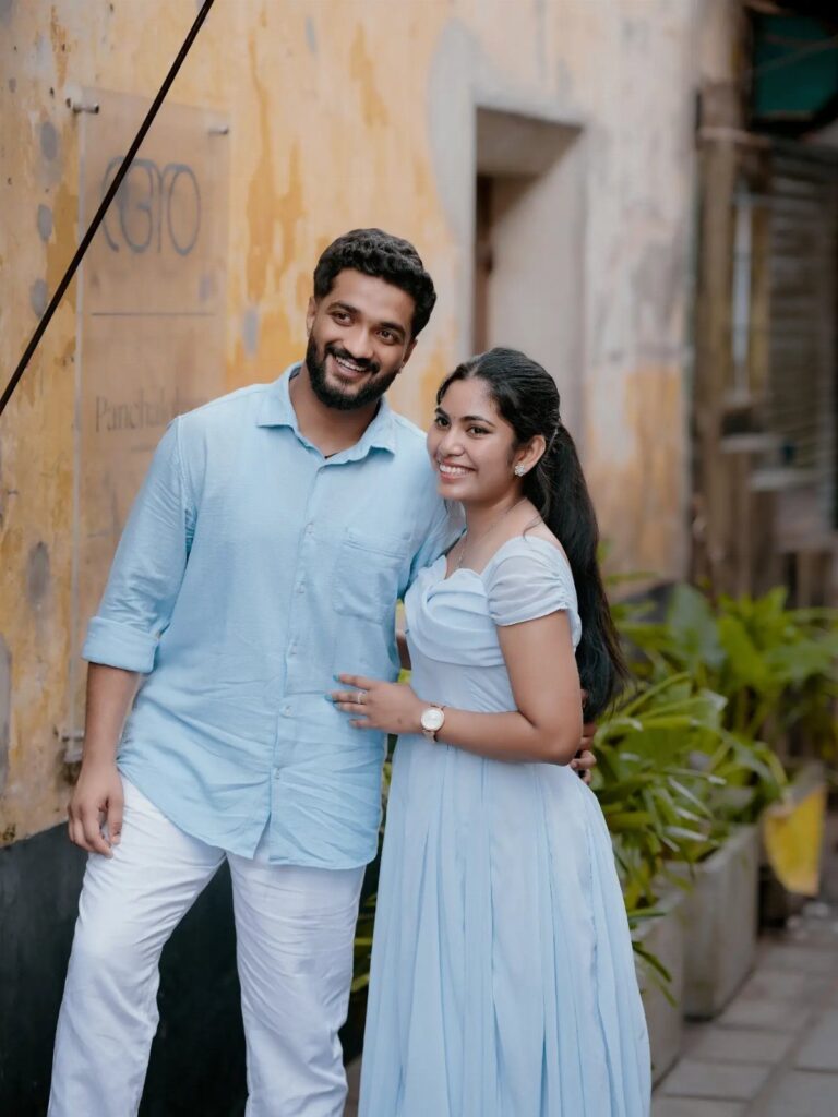 Couple in matching light blue outfits posing against a yellow wall for a photoshoot.