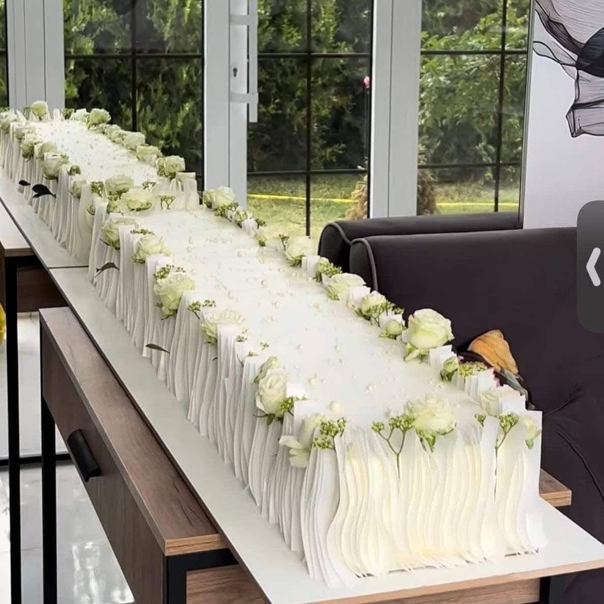Long rectangular white wedding cake with pleated frosting and white rose decorations.