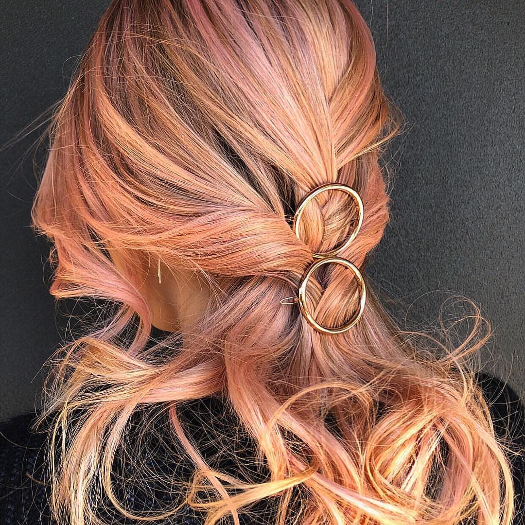 Rose-gold wavy hair in a side ponytail secured with two gold metal rings.
