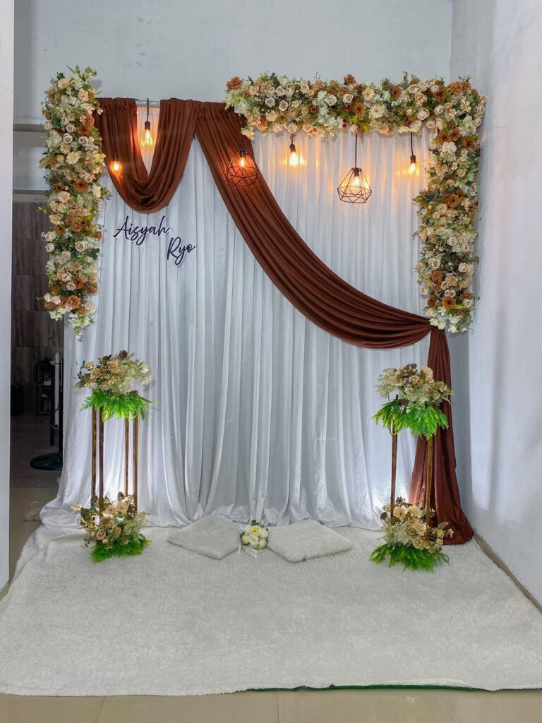 Wedding backdrop with white curtains, brown fabric draping, and white floral arrangements.