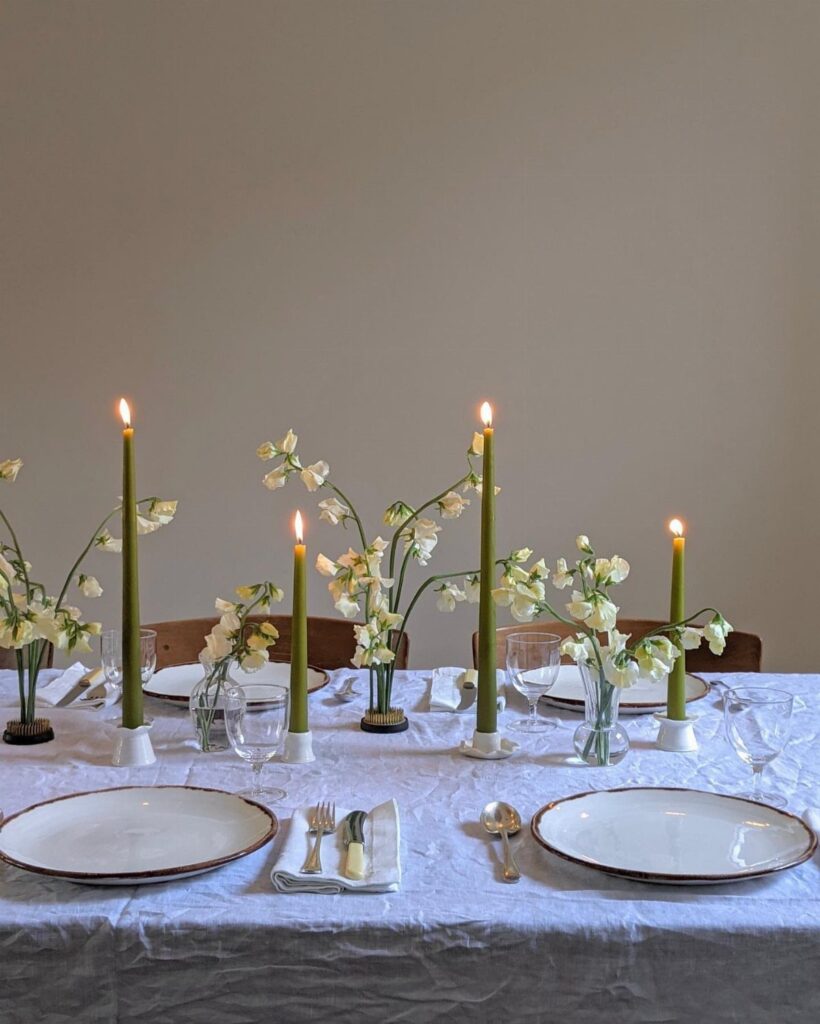 Minimalist tablescape with white plates, green taper candles, and white flowers on linen.