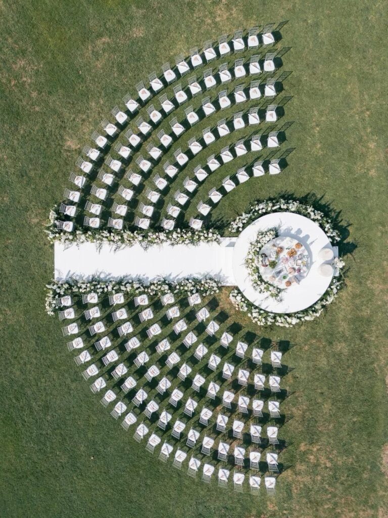 White wedding chairs arranged in concentric semi-circles around a circular floral altar platform.