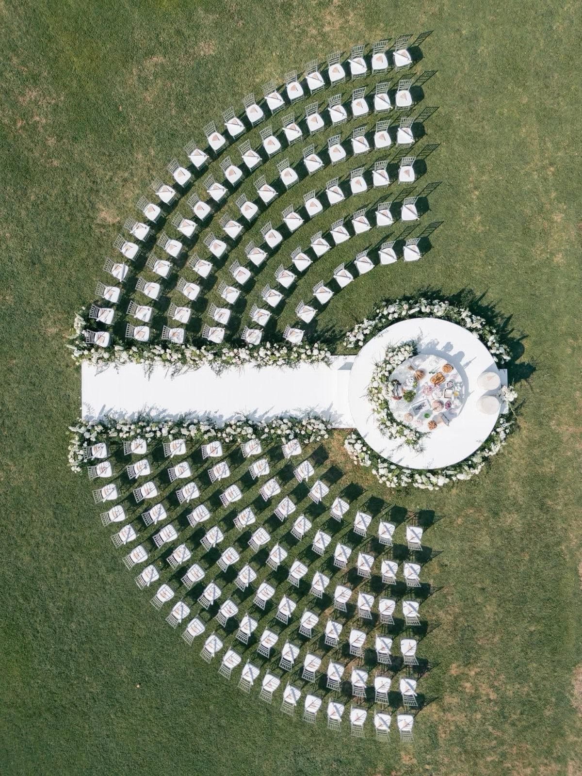 White wedding chairs arranged in concentric semi-circles around a circular floral altar platform.
