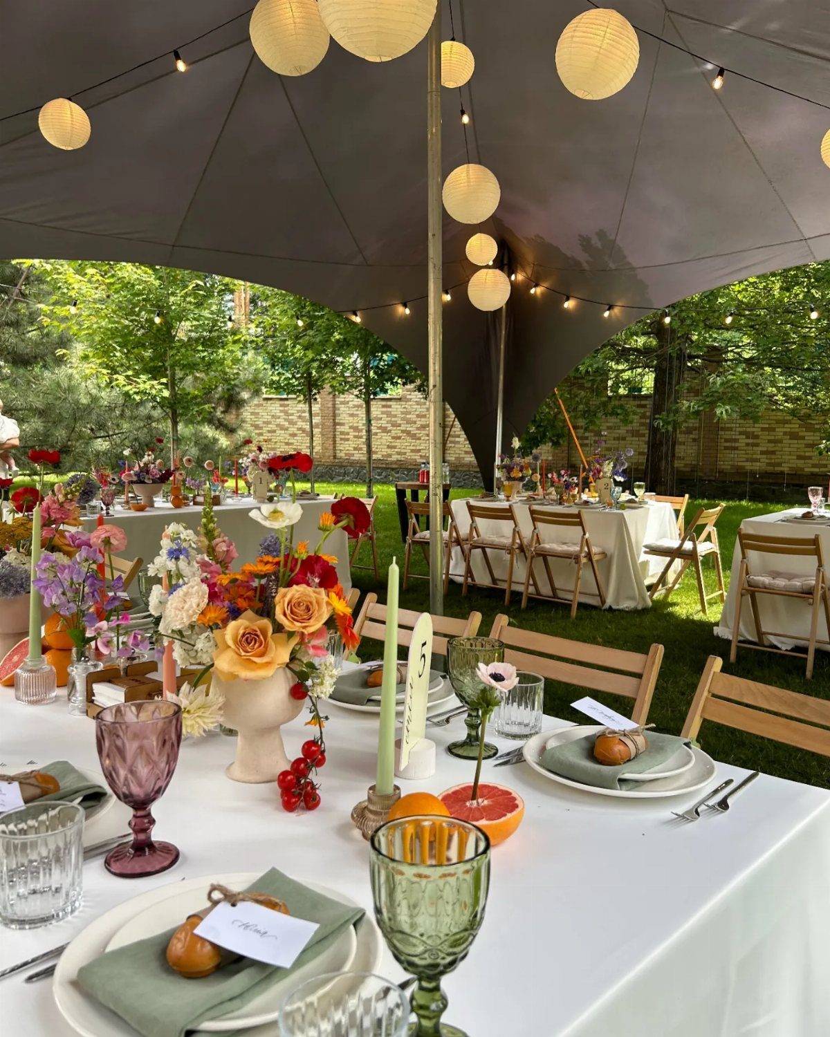 Outdoor wedding reception under a grey stretch tent with floral centerpieces and lanterns.