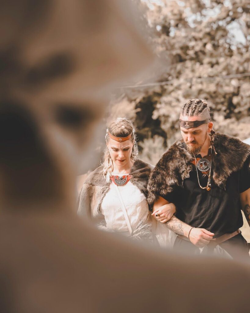Viking couple in fur capes and traditional jewelry walking together outdoors.