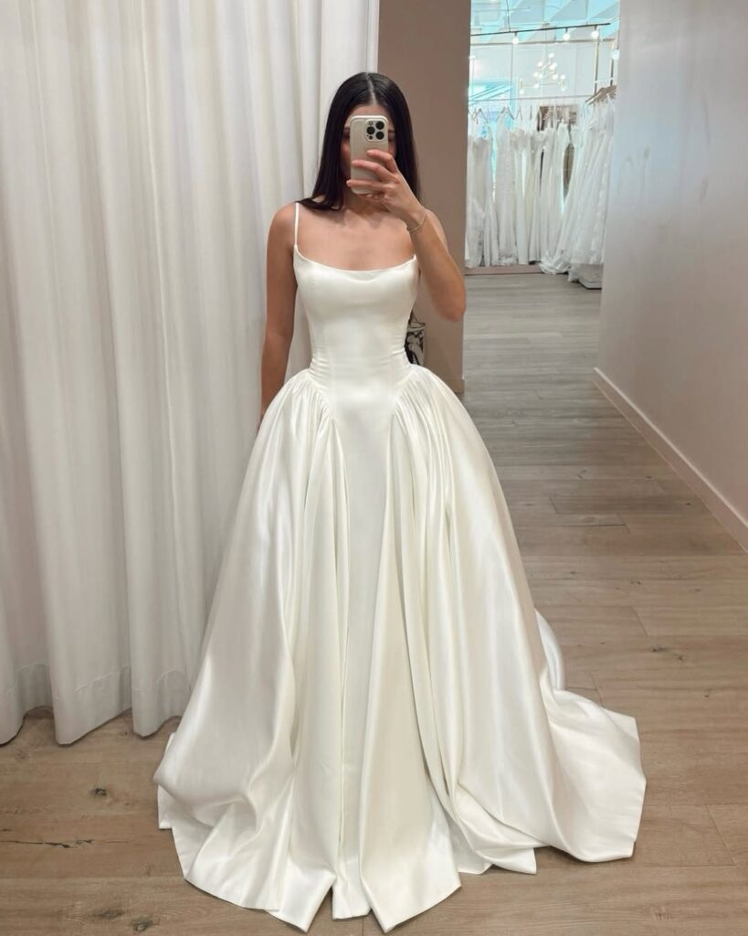 Woman wearing a white satin basque waist ball gown wedding dress in a boutique.