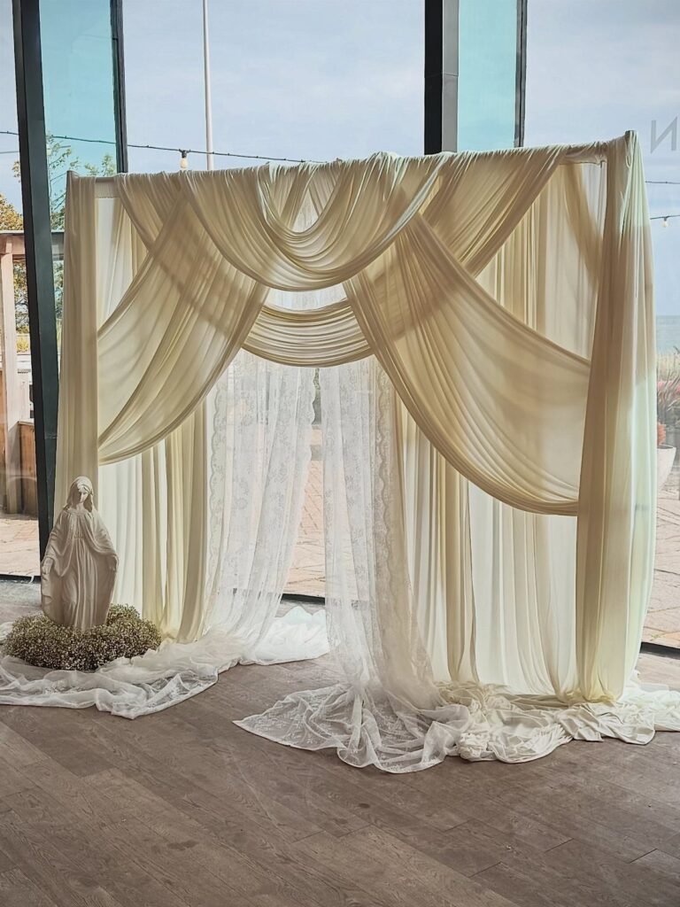 Cream fabric draped backdrop with lace accents and a small white statue.