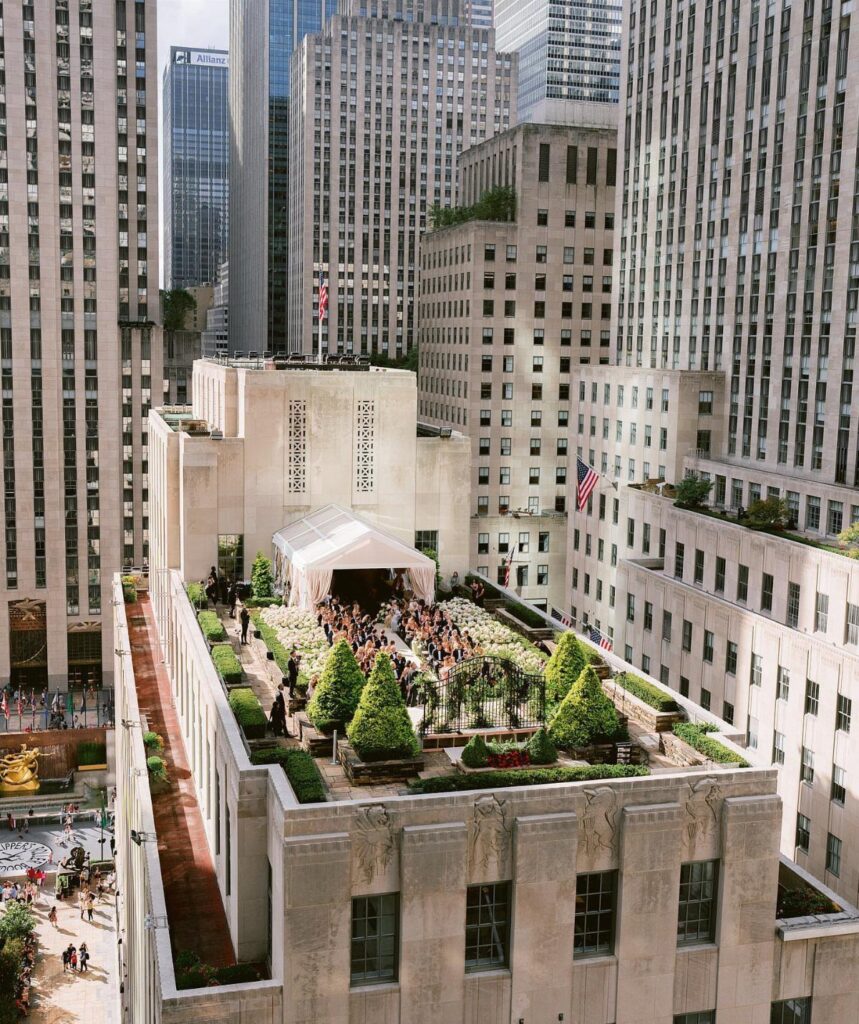 Rooftop garden with a white tent and guests surrounded by tall city skyscrapers.
