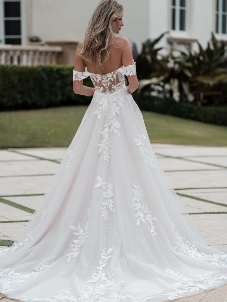 Woman wearing a white A-line wedding dress with lace floral embroidery and long train.