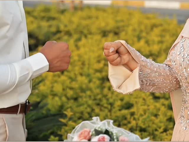 Man and woman in formal attire bumping fists with a floral background