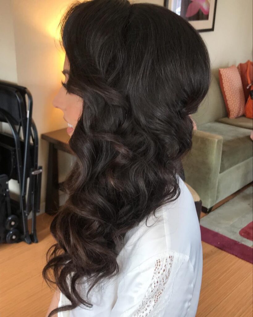 Woman with dark brown hair styled in voluminous side-swept waves over one shoulder.