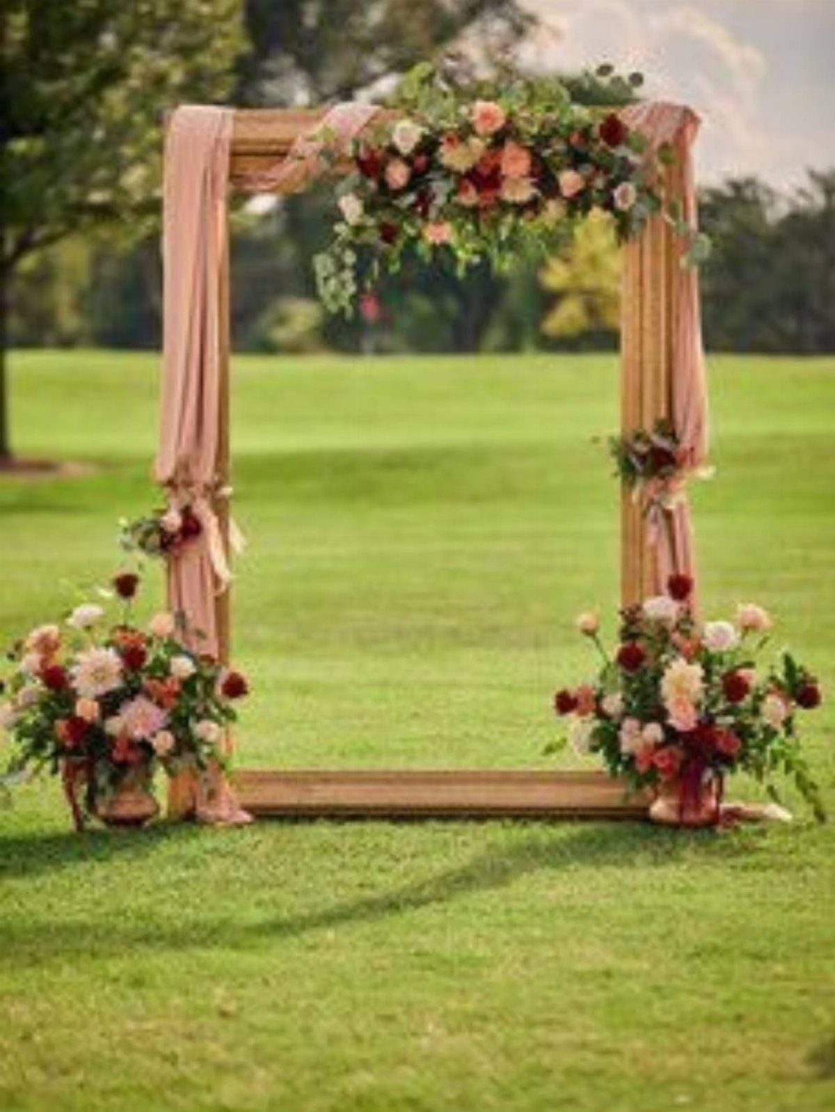 Gold decorative frame with pink fabric and floral arrangements on a green lawn