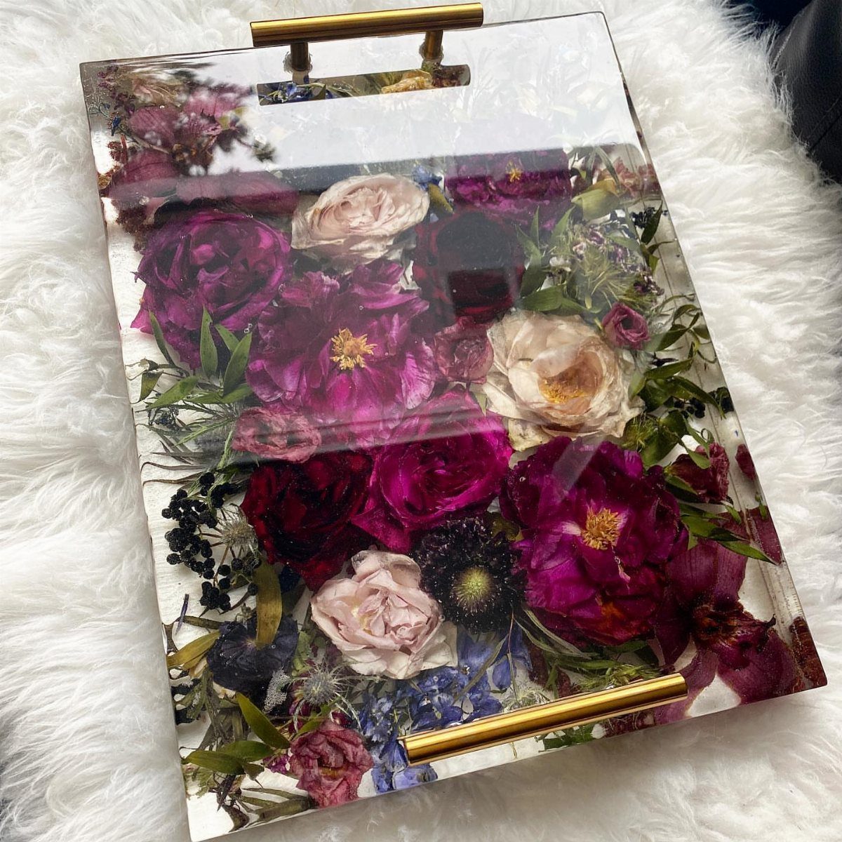 Acrylic tray with gold handles containing pressed pink and purple wedding flowers.