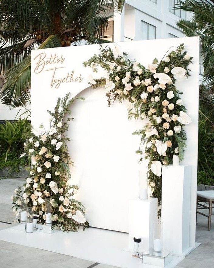 White floral wedding backdrop with gold lettering and candles on white pedestals.
