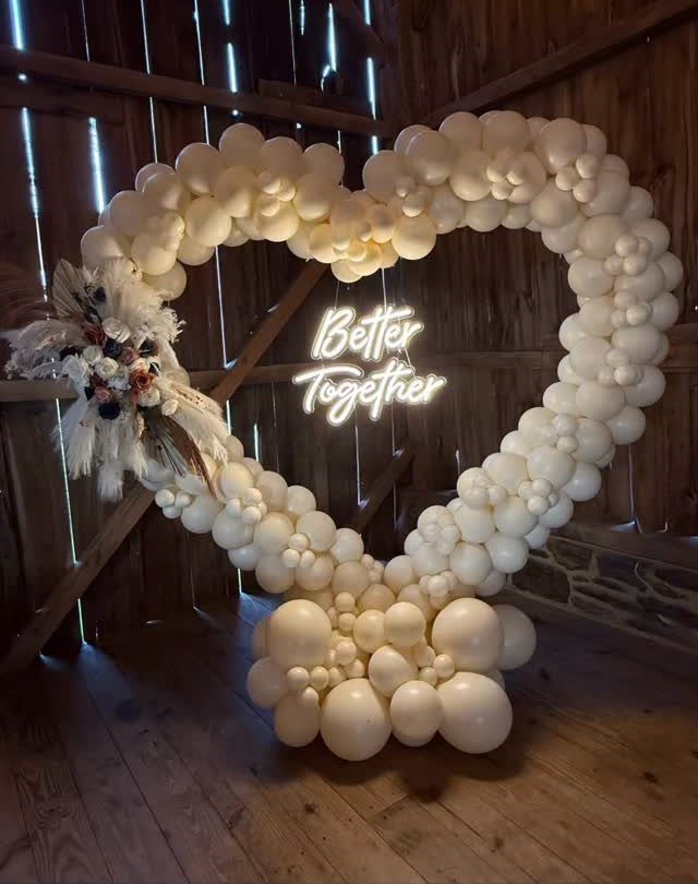 Heart-shaped cream balloon arch with a Better Together neon sign in a wooden barn.