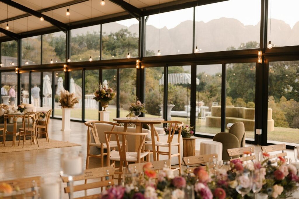 Modern glass-walled event venue with wooden furniture and mountain views for a wedding.